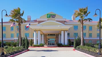 A Holiday Inn Express & Suites hotel with a central entrance, palm trees, and a clear blue sky.