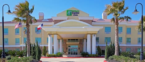 A Holiday Inn Express & Suites hotel with a central entrance, palm trees, and a clear blue sky.