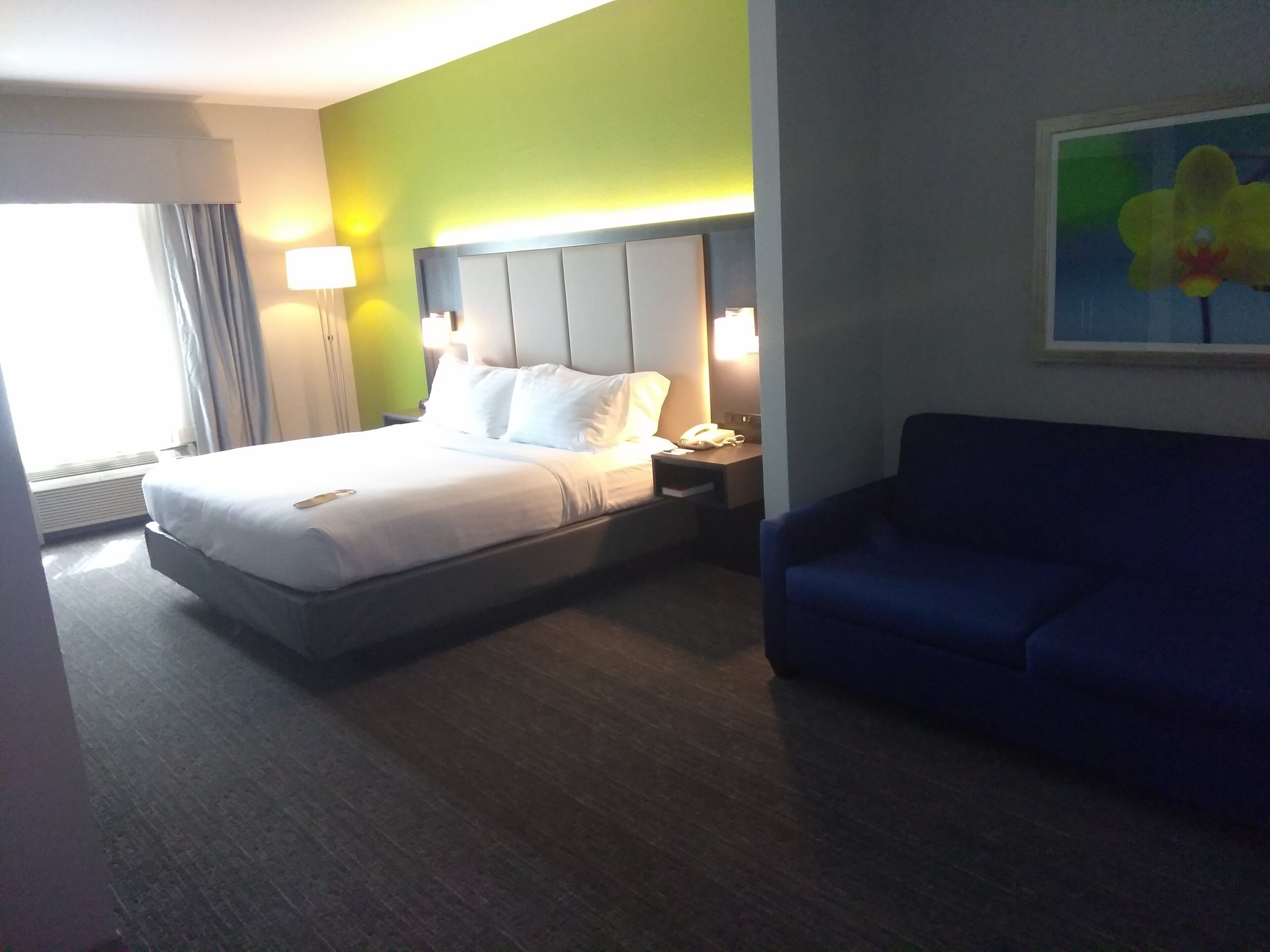 Una habitación de hotel con una cama, mesitas de noche, un sofá azul y un cuadro en la pared.
