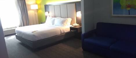 Una habitación de hotel con una cama, mesitas de noche, un sofá azul y un cuadro en la pared.