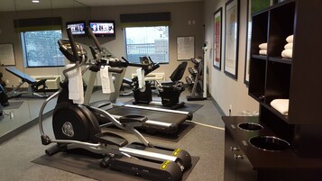 Un gimnasio con cintas de correr, bicicletas estáticas y un espejo grande.