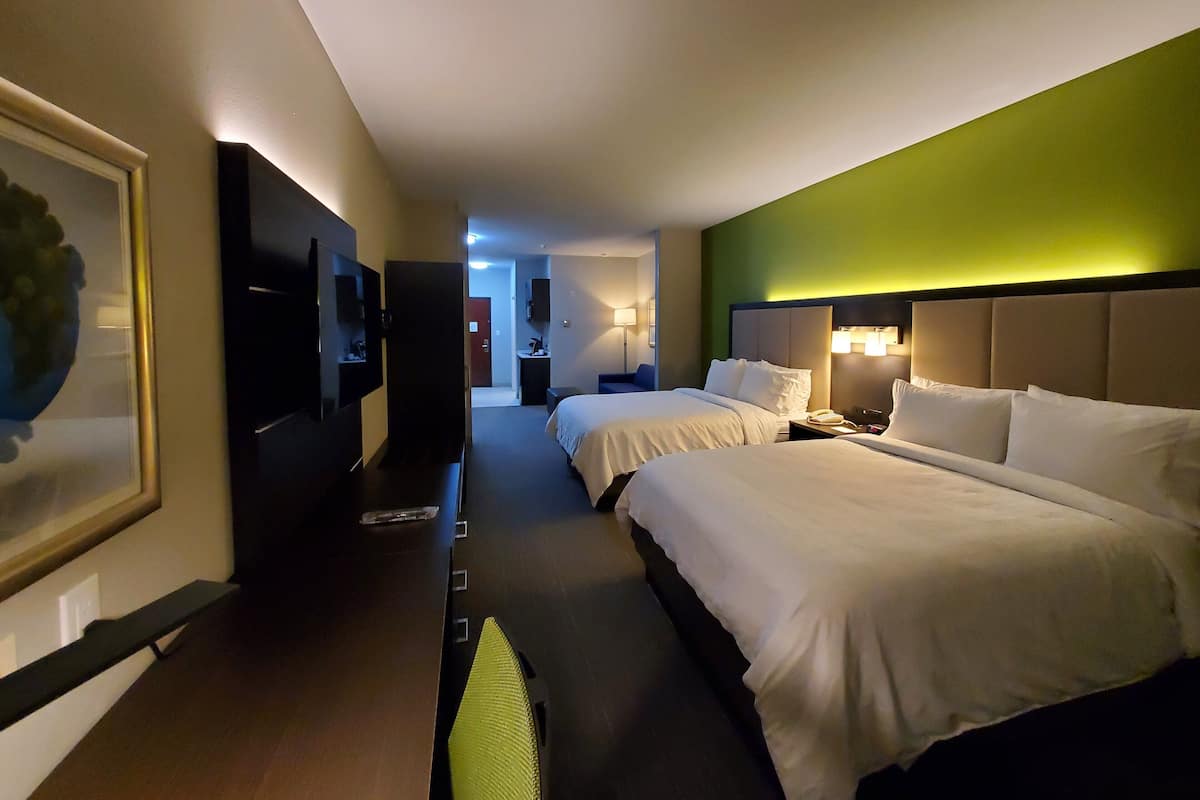 A hotel room with two beds, a TV, a desk, and a green accent wall.