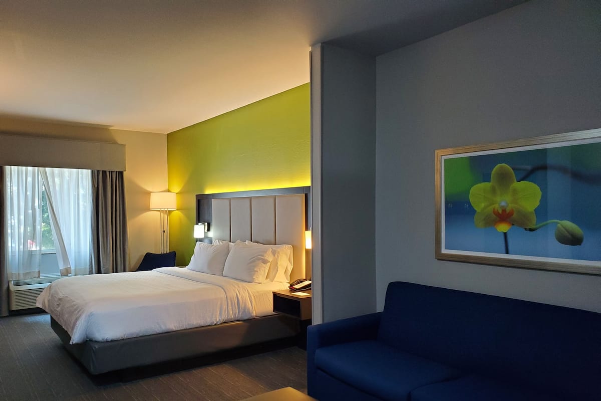 A hotel room with a bed, a blue sofa, a painting of an orchid, a nightstand, and a lamp.