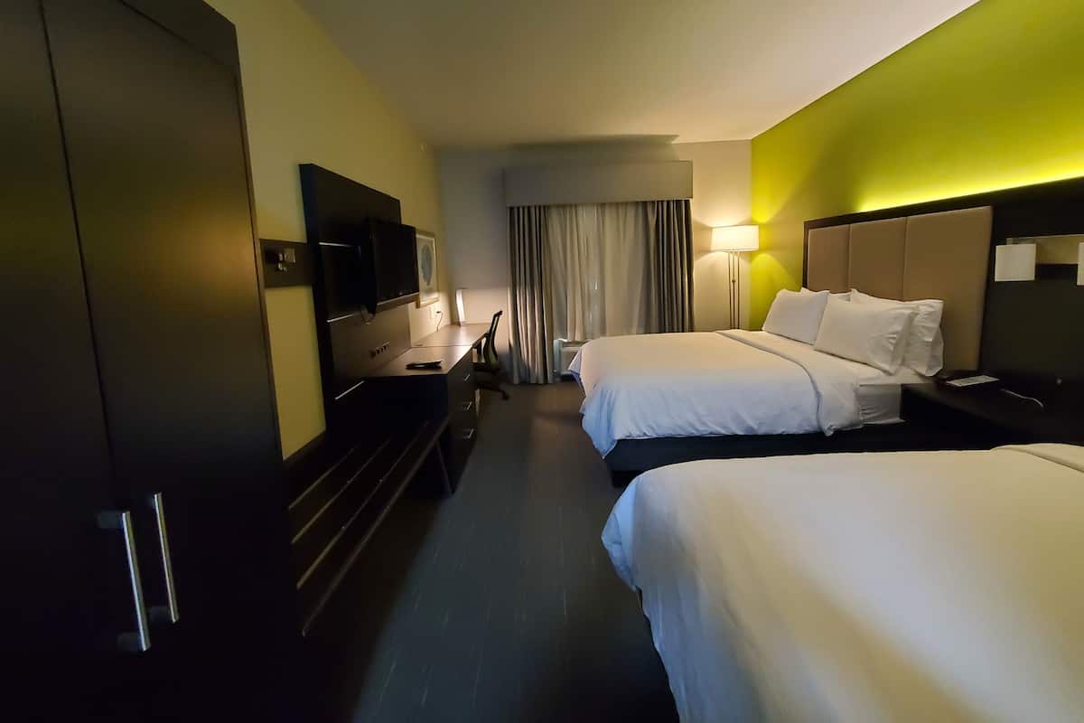 A hotel room with two beds, a desk with a TV, a lamp, and a window with curtains.