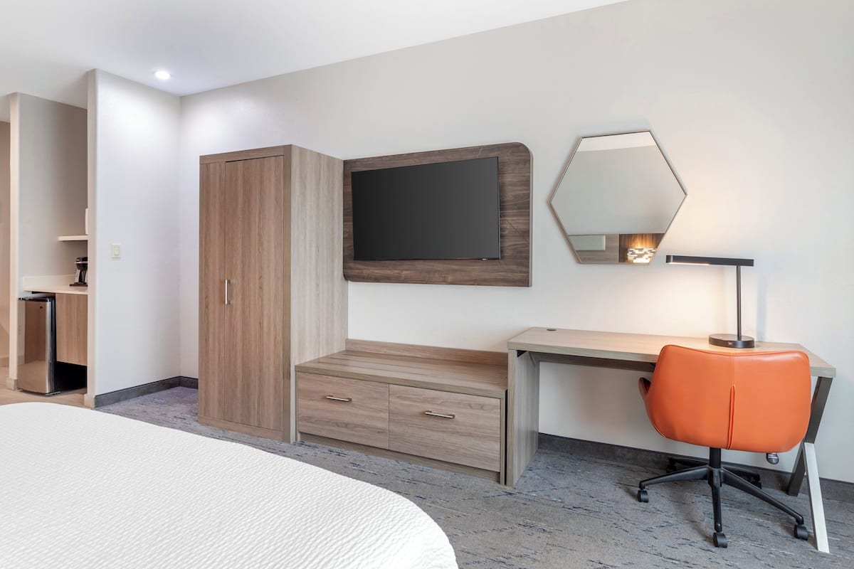 Une chambre d’hôtel comprenant un lit, un bureau avec une chaise, une armoire, un miroir et une petite table avec une lampe.