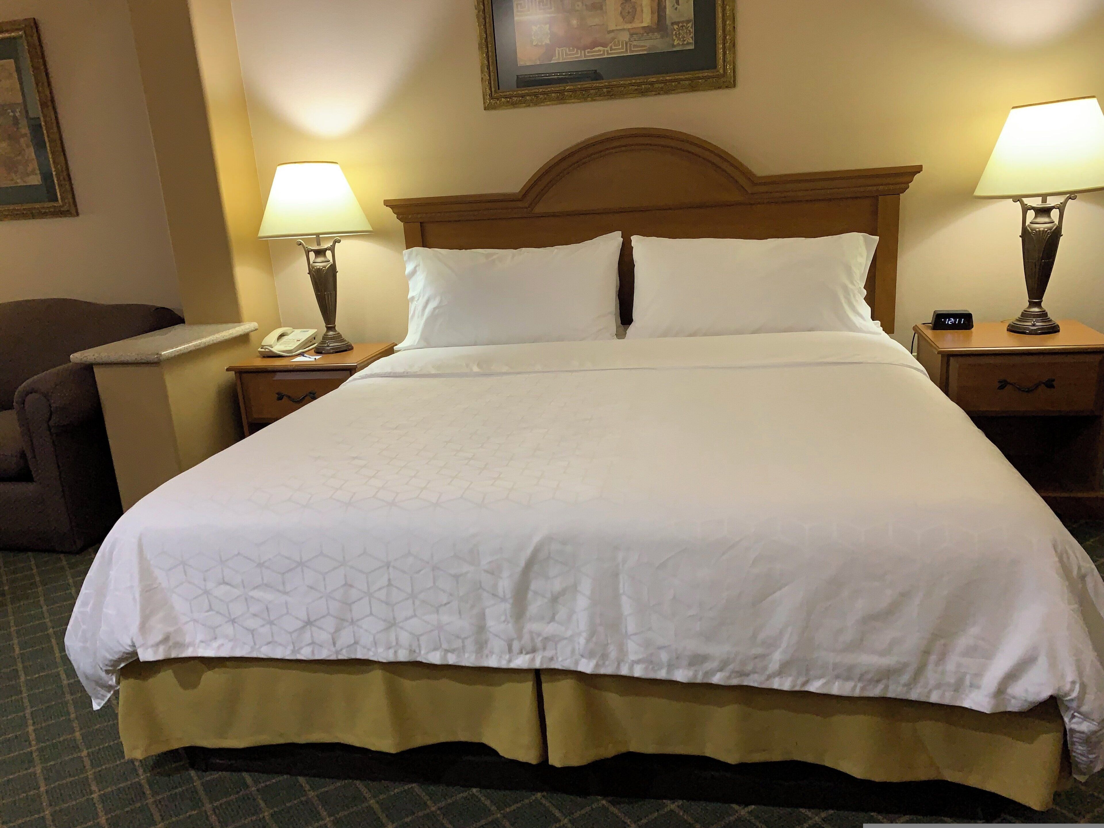 A hotel room with a large bed, two bedside lamps, a nightstand with a telephone, and a chair.