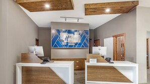 A reception area with two white reception desks, a blue and white geometric wall art, and wooden accents on the ceiling and furniture. - Holiday Inn Express & Suites Alice by IHG (Alice)
