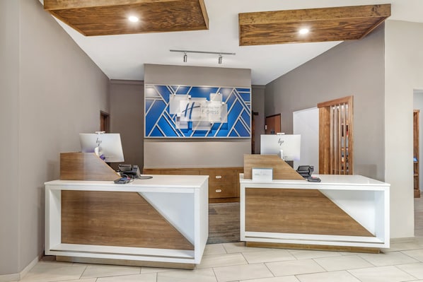A reception area with two white reception desks, a blue and white geometric wall art, and wooden accents on the ceiling and furniture.