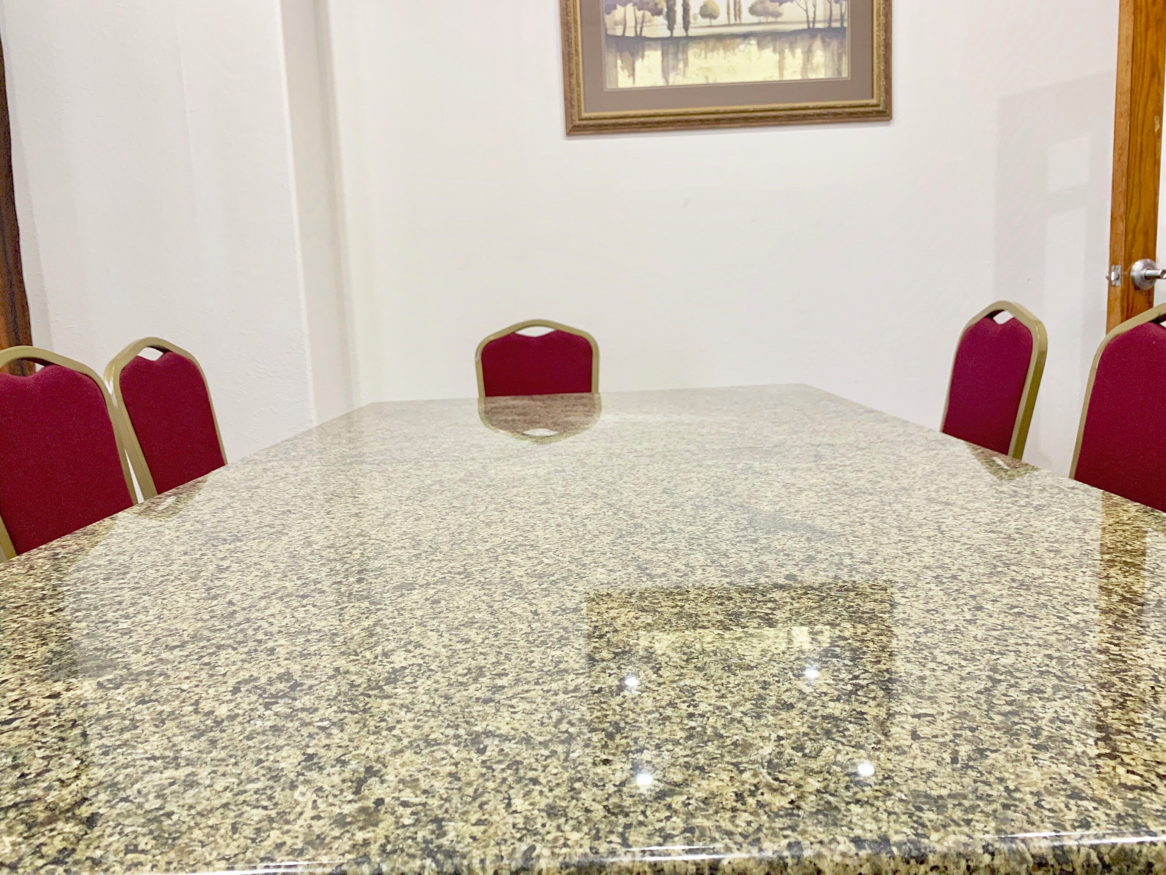 A conference room with a granite table and red upholstered chairs.