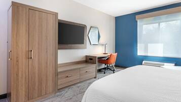 A hotel room with a bed, a desk, an orange chair, a wardrobe, and a large window.