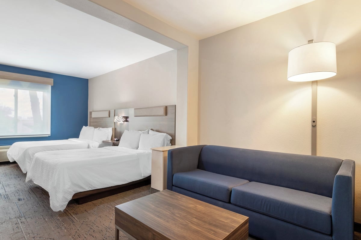 Une chambre d’hôtel avec deux lits, un canapé bleu, une table basse en bois et une lampe fixée au mur.