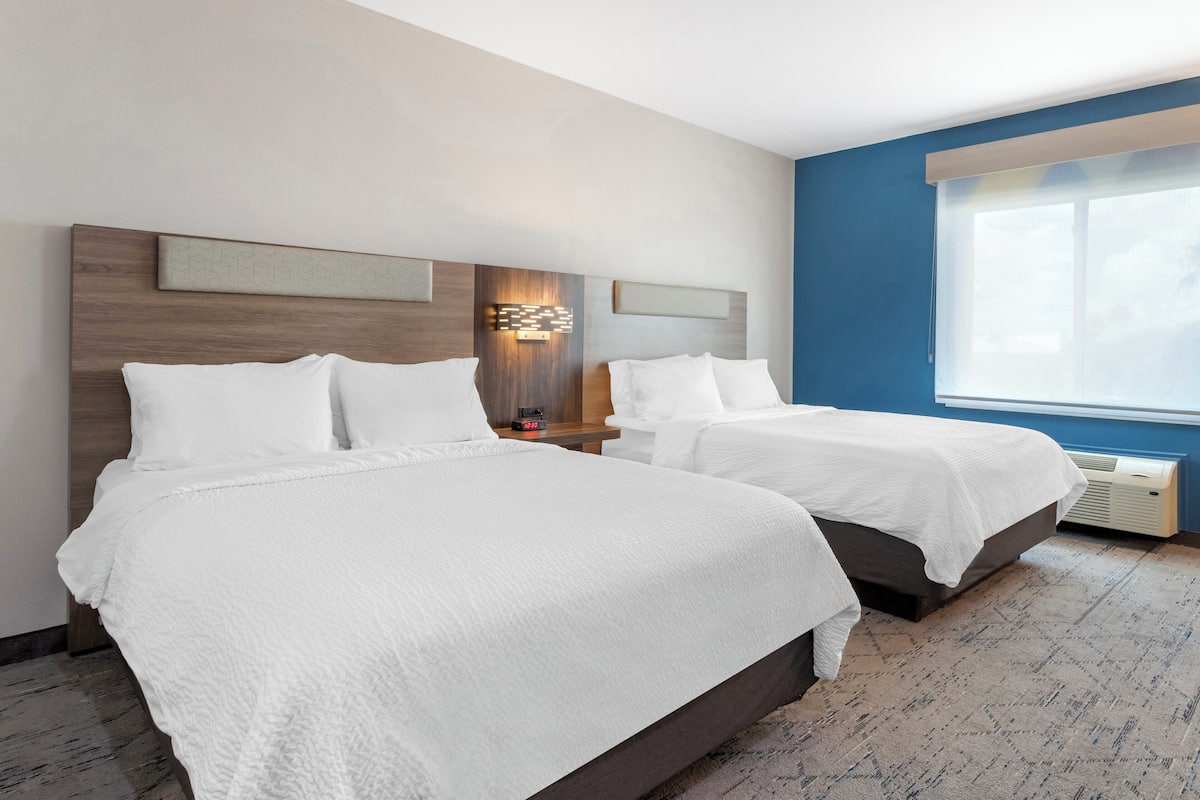 Une chambre d’hôtel avec deux lits, une tête de lit en bois, une lampe fixée au mur et une grande fenêtre.