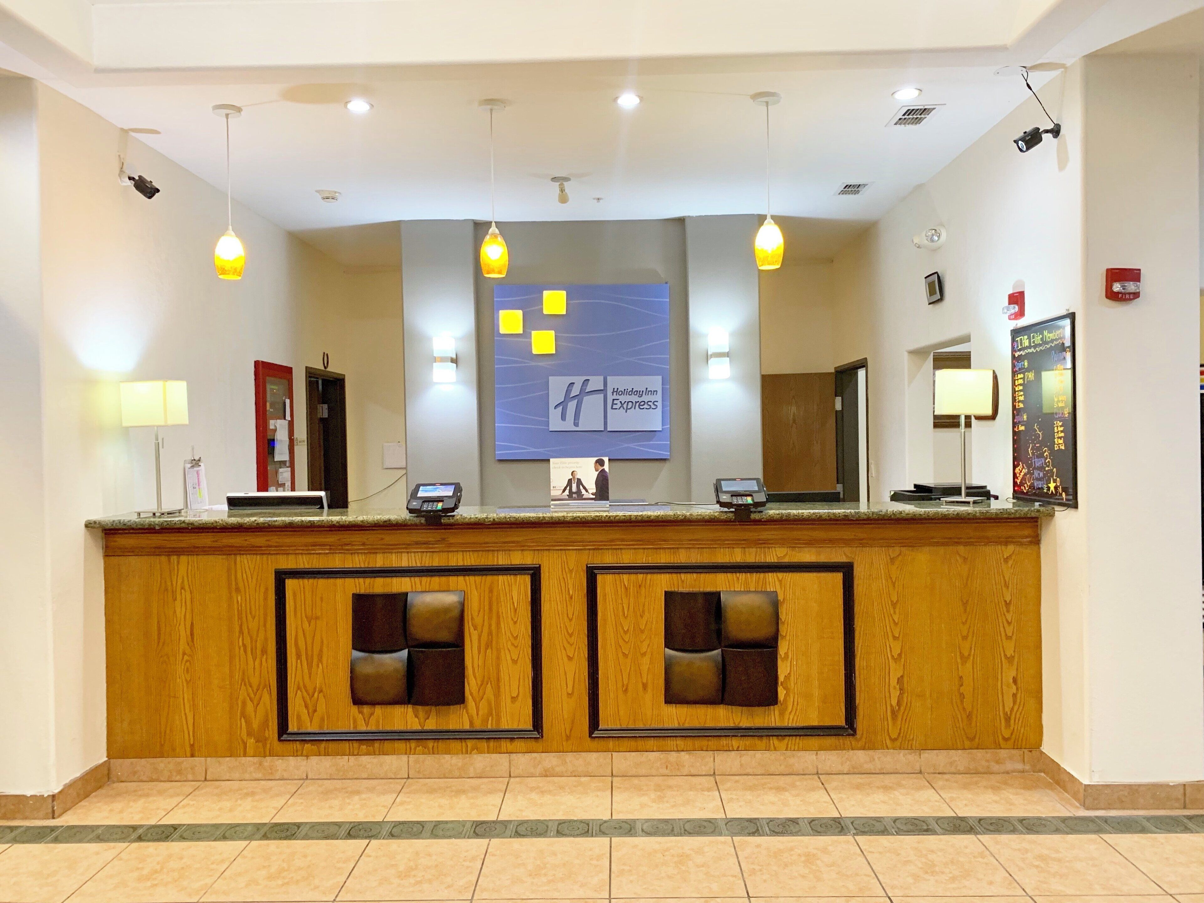Una recepción de hotel con una estación de registro digital, un letrero grande de Holiday Inn Express y un detector de incendios en la pared.