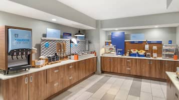 A modern cafe with a coffee machine, fruit and bakery display, and a sign reading "FEELIN' FRESH THIS MORNING?"