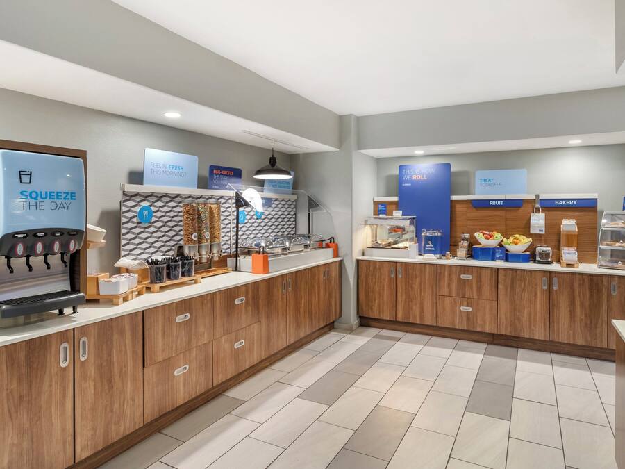 A modern cafe with a coffee machine, fruit and bakery display, and a sign reading "FEELIN' FRESH THIS MORNING?"