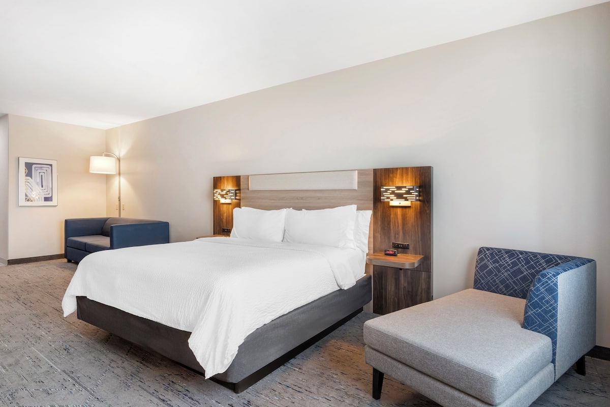 Une chambre d’hôtel avec un grand lit, un fauteuil bleu, un petit canapé et deux lampes fixées au mur.