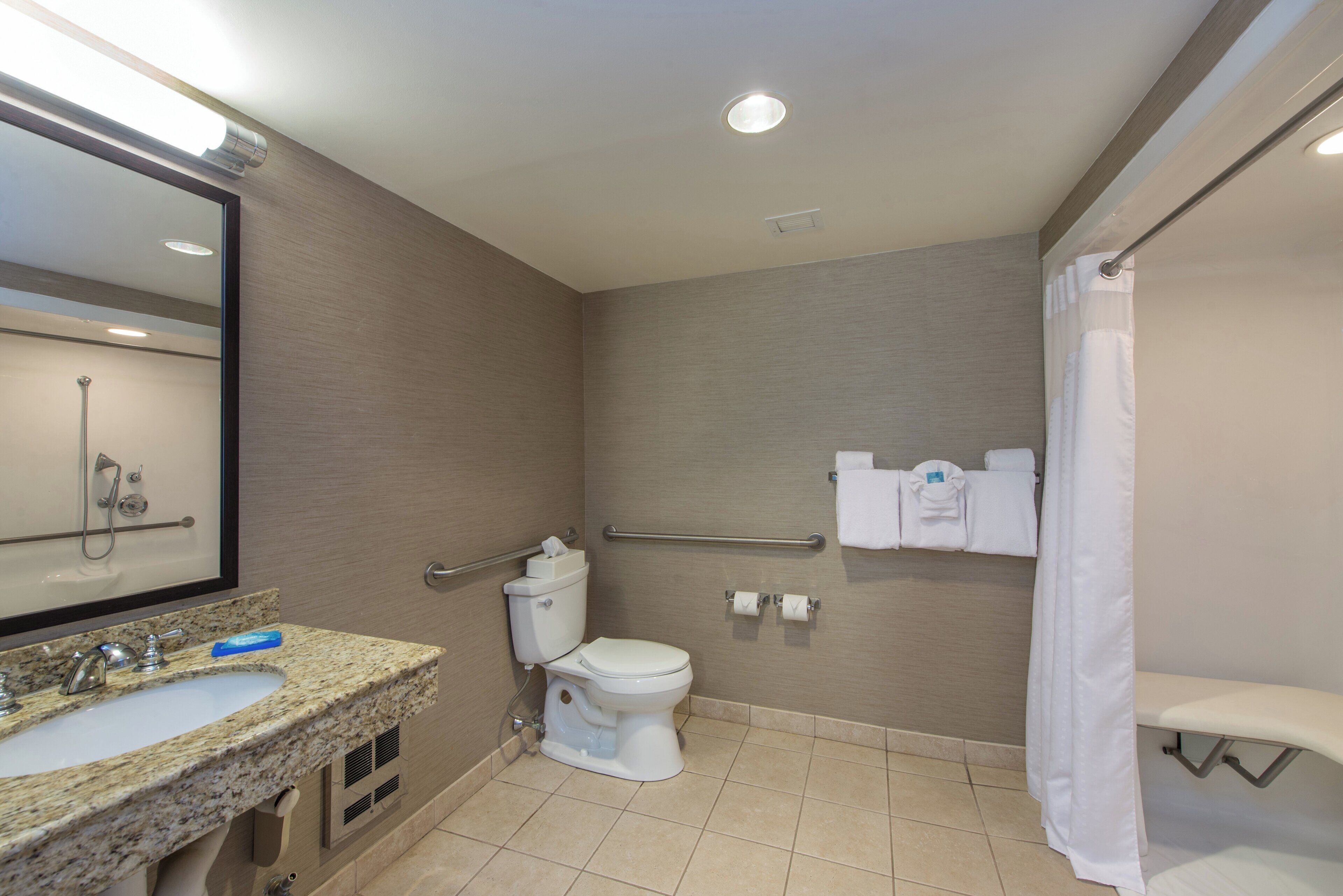 Un baño con lavamanos, inodoro, ducha y barras de apoyo.
