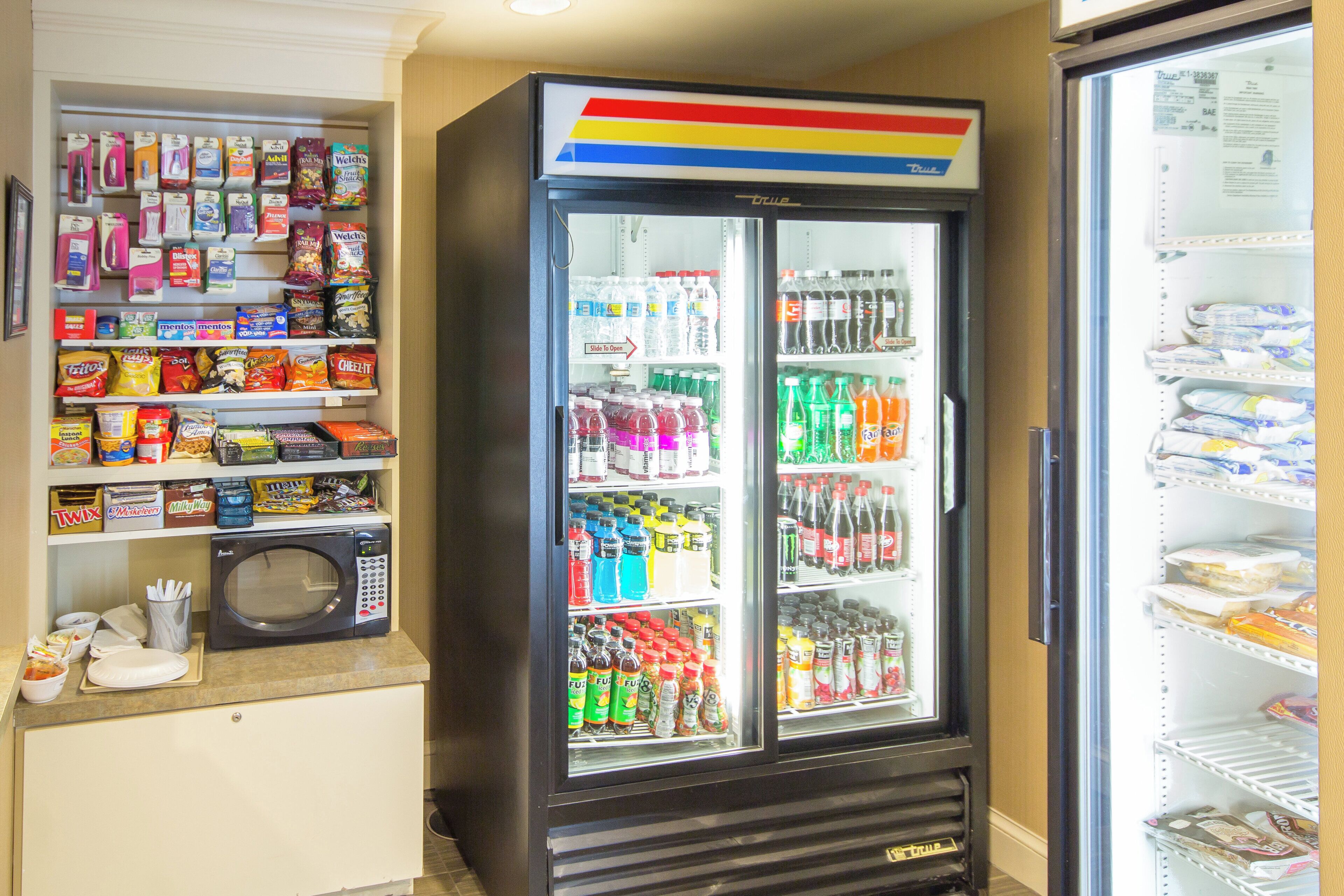 A vending machine stocked with snacks and drinks, a microwave, and a refrigerator with various food items.