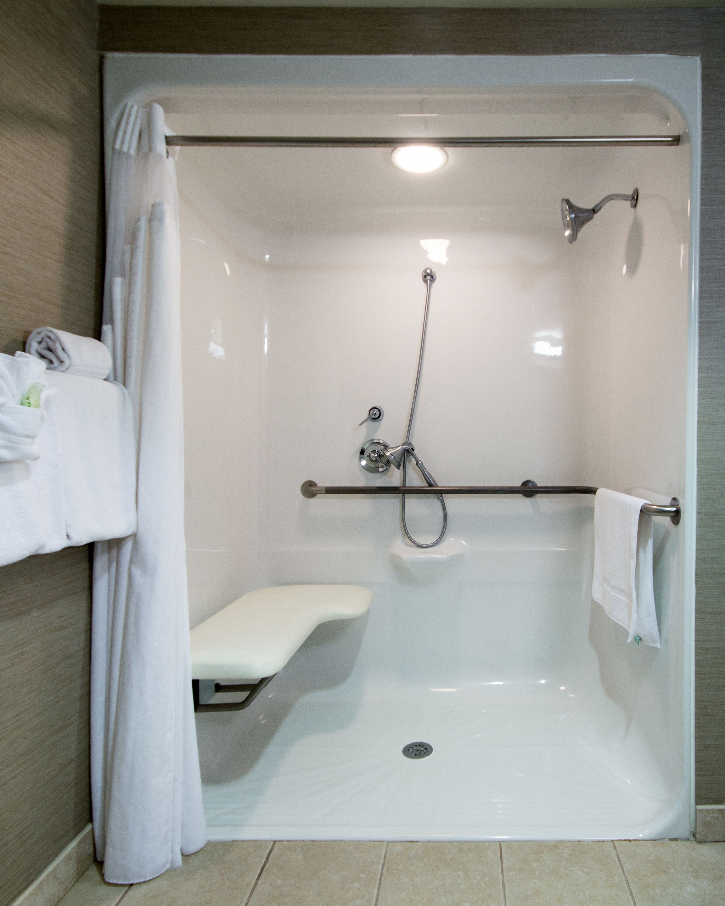 A modern bathroom with a walk-in shower, a bench, and a towel rack.