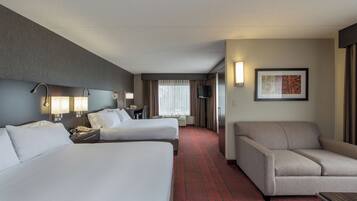 A hotel room with two beds, a sofa, a desk with a telephone, a television, and a framed picture on the wall.