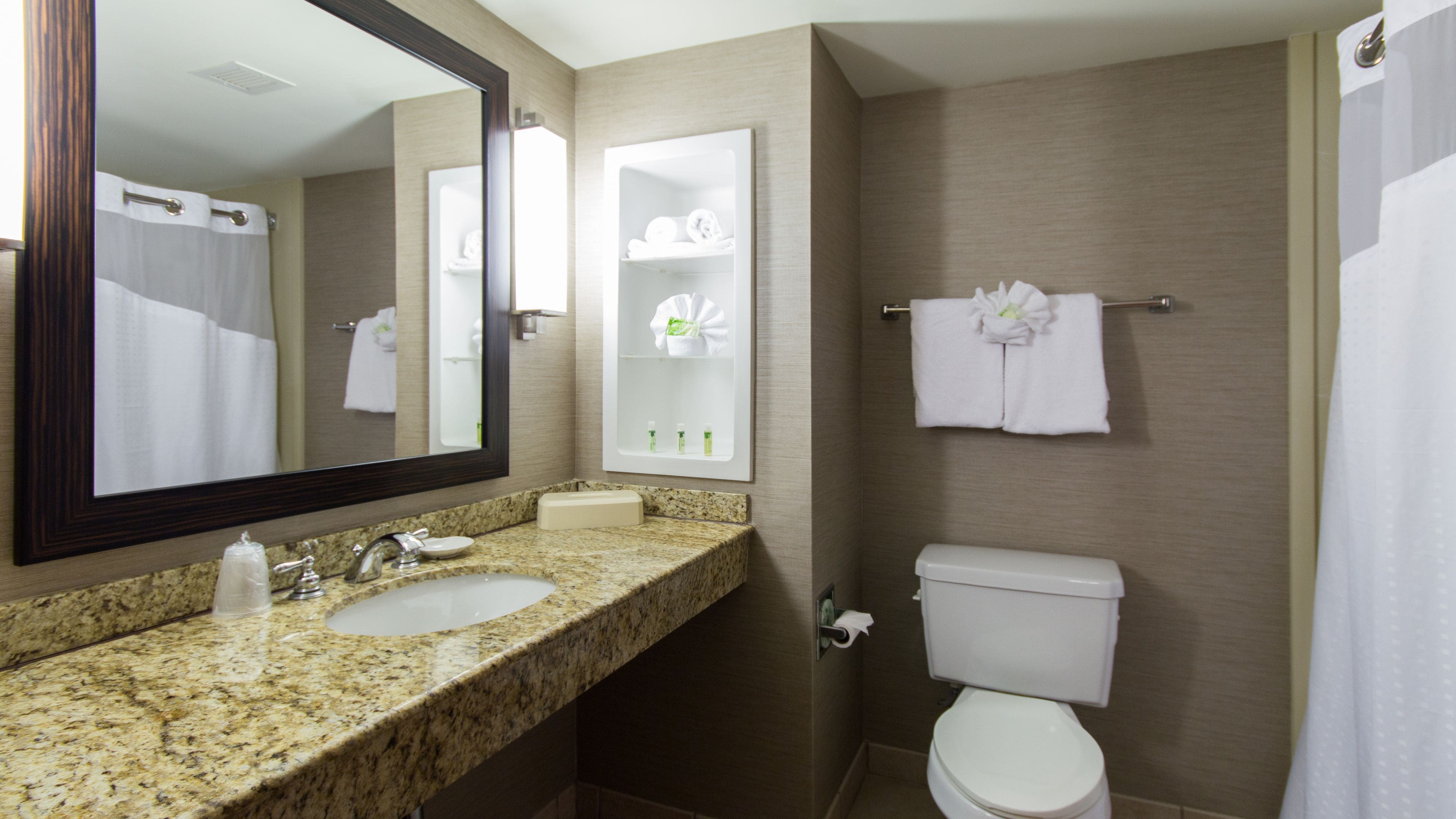 A bathroom with a granite countertop, a sink, a mirror, a toilet, and a towel rack with a folded towel.