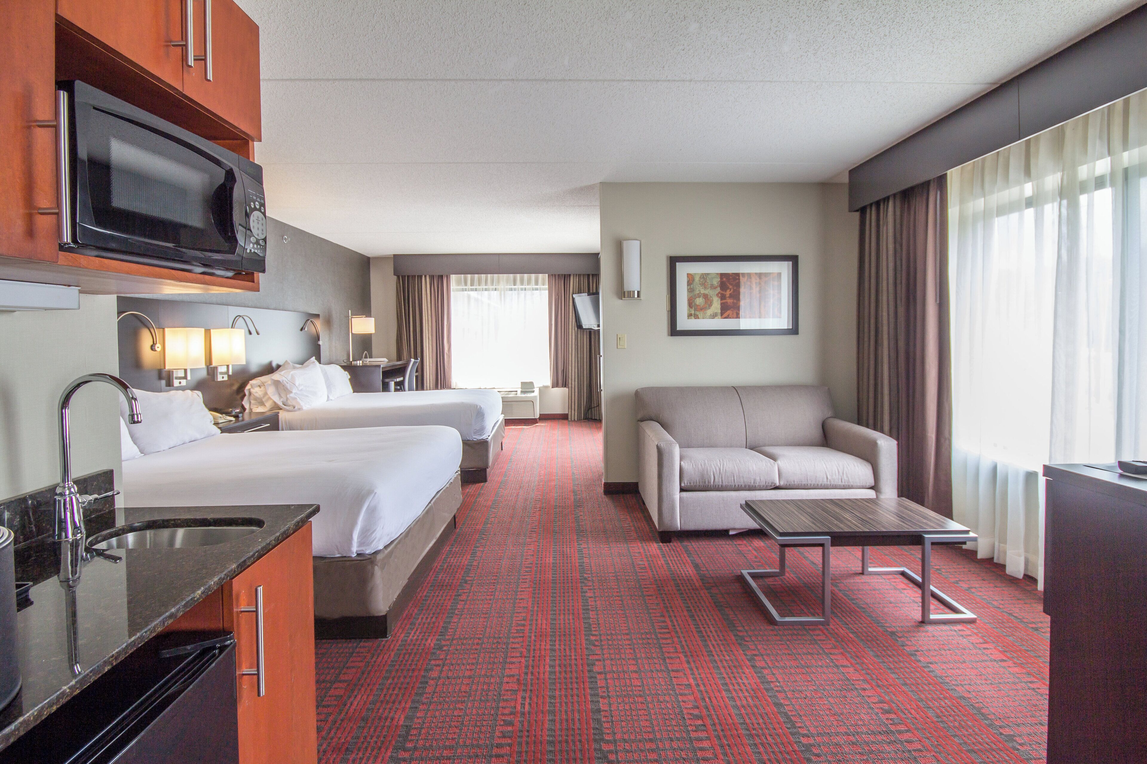 A hotel room with a bed, a sofa, a TV, and a desk with a sink.