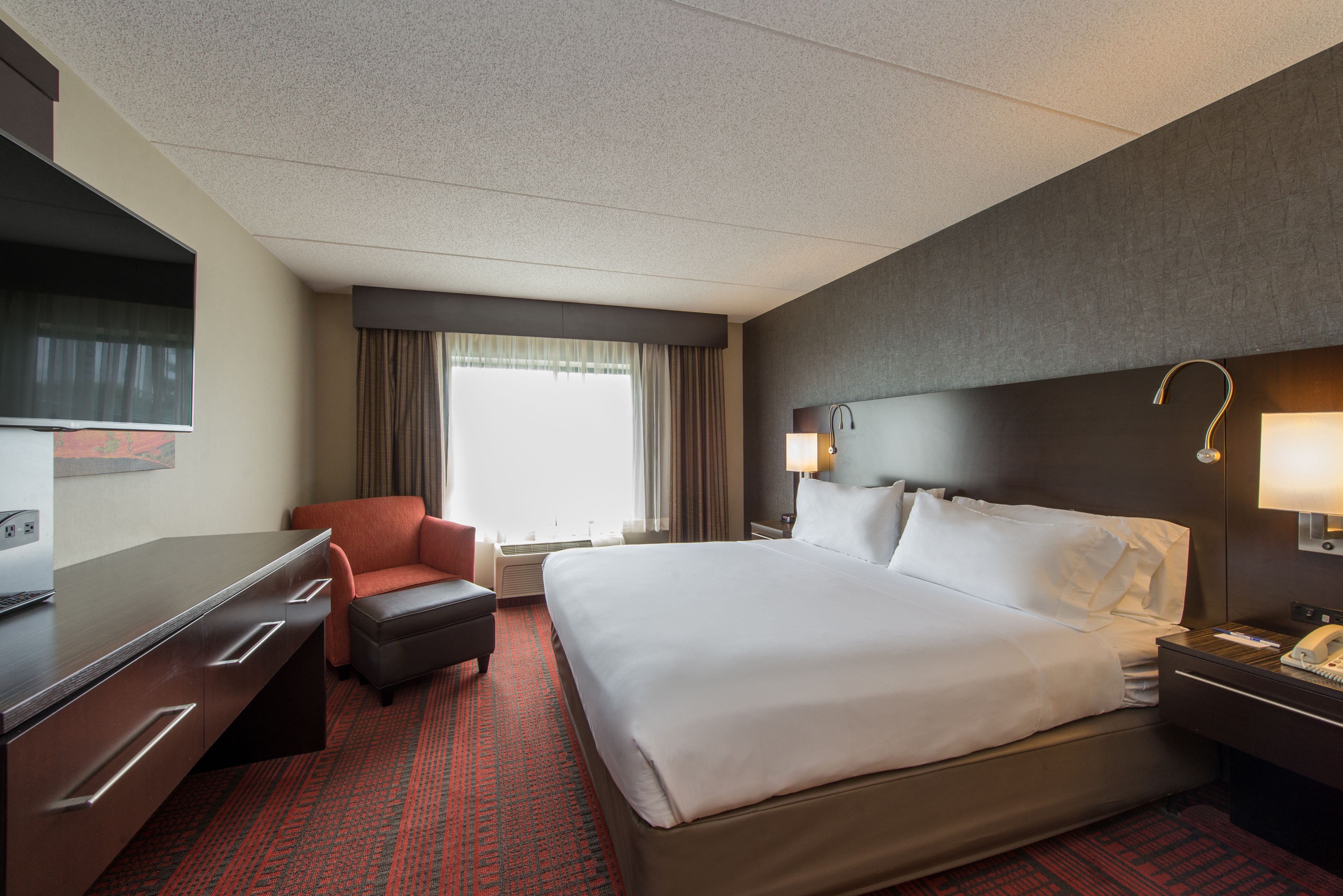 A hotel room with a bed, a desk, a chair, a TV, and a window with curtains.