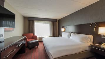 A hotel room with a bed, a desk, a chair, a TV, and a window with curtains.