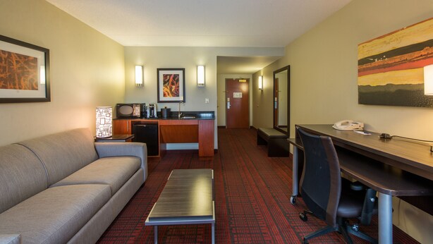 A hotel room with a sofa, a desk, a small table, a kitchenette, and a hallway with a painting. - Holiday Inn Express Hotel & Suites Auburn by IHG (Auburn)