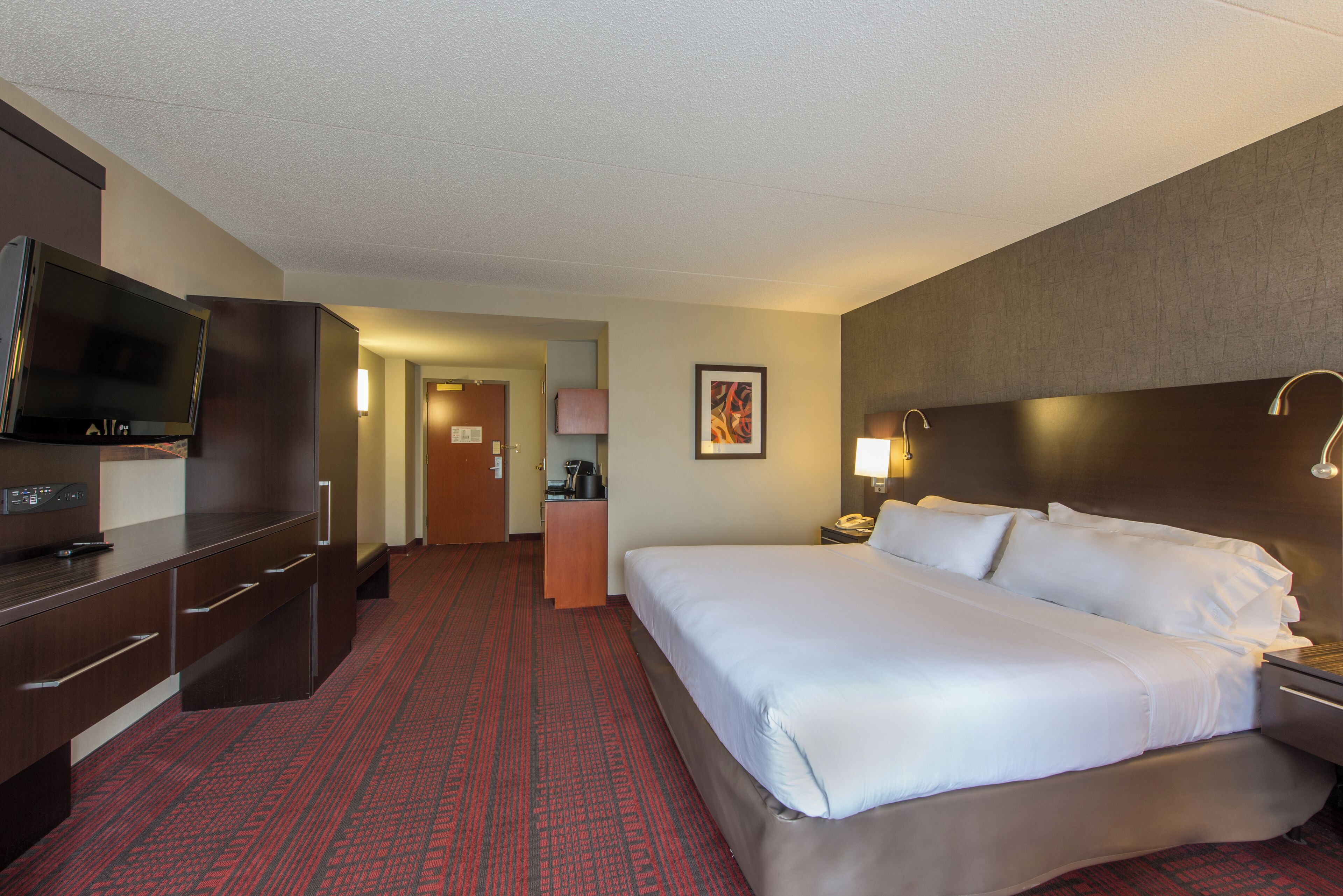 A hotel room with a large bed, a desk with a flat-screen TV, a coffee machine, and a telephone.