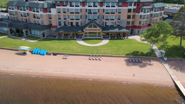 A multi-story hotel with a central courtyard, outdoor seating area, and a beach area with lounge chairs. - SouthShore Hotel on Lake Bemidji, Trademark Coll by Wyndham (Bemidji)