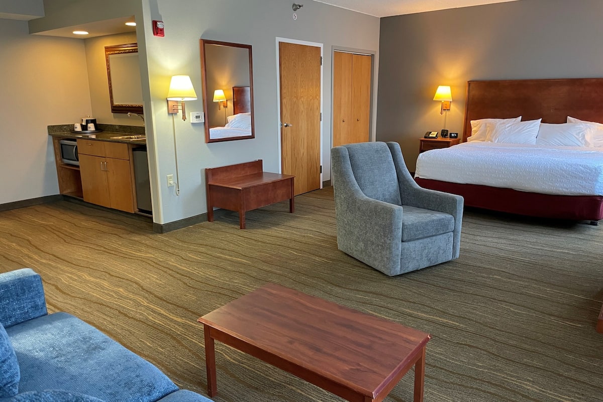 A hotel room with a bed, a chair, a small table, a sofa, a desk with a computer, and a mirror.