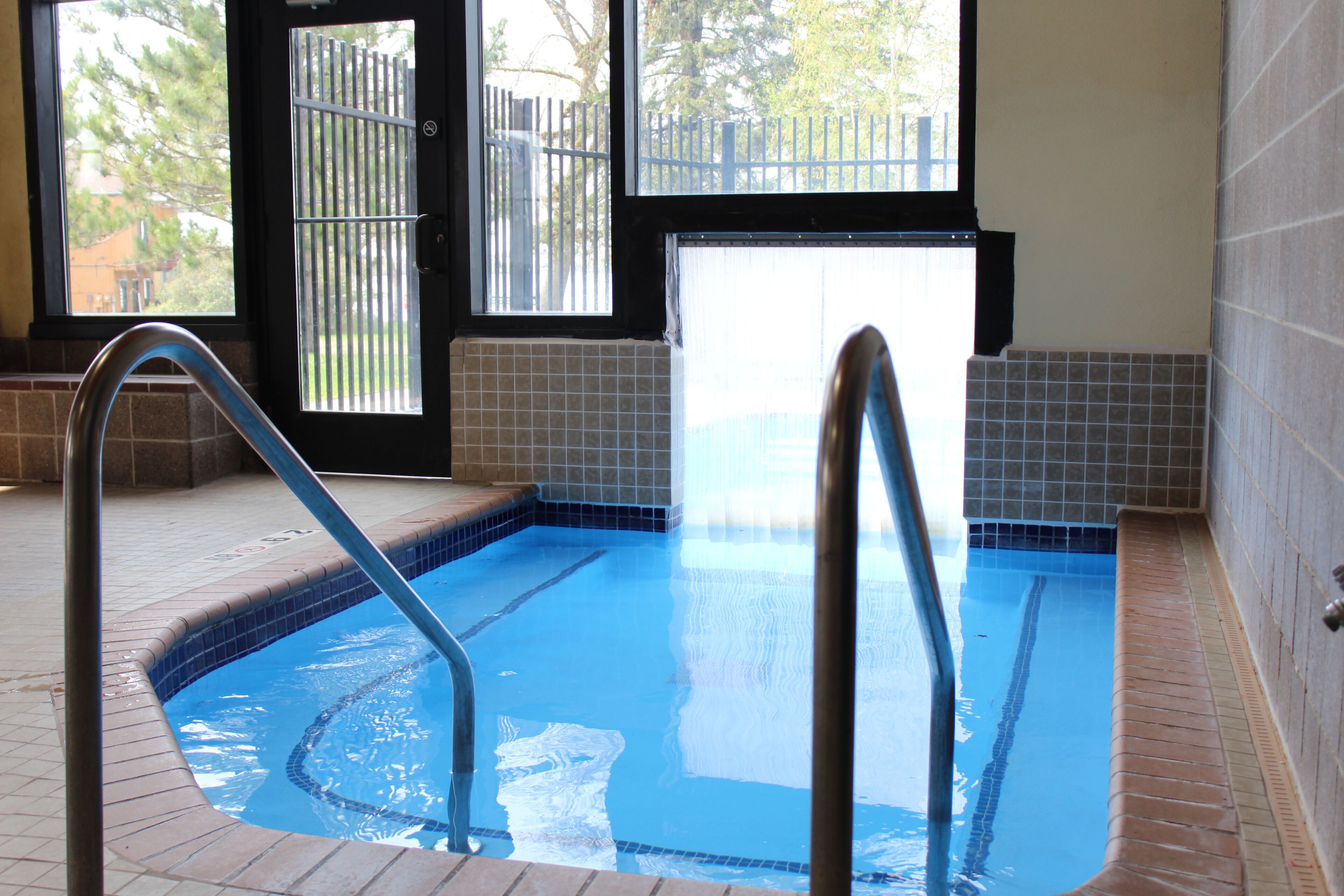 A swimming pool with a metal ladder, tiled walls, and a door leading outside.