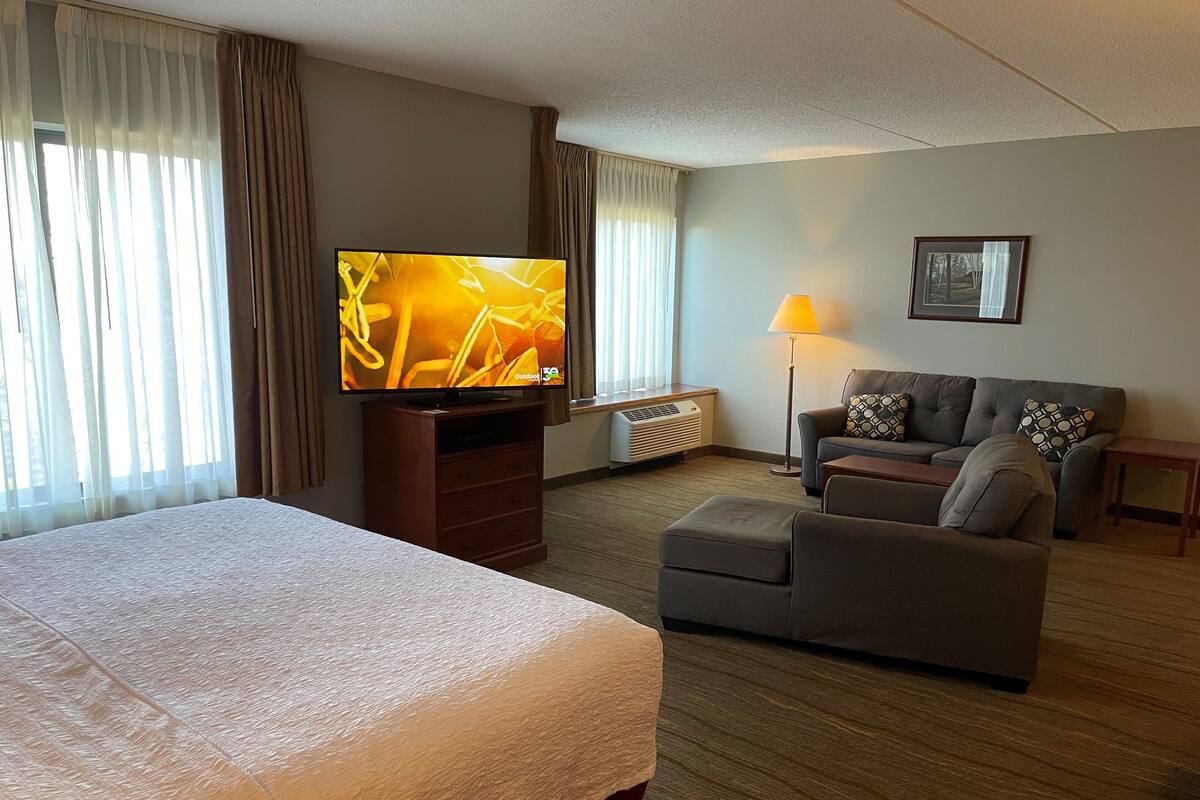 A hotel room with a bed, a television, a sofa, and a lamp.