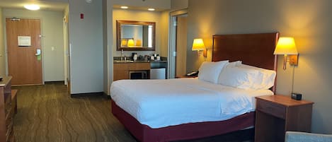 A hotel room with a large bed, bedside lamps, a desk, and a bathroom visible through an open door.