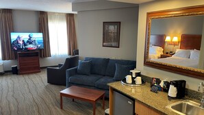 A hotel room with a TV, sofa, coffee table, kitchenette, and a large mirror. - SouthShore Hotel on Lake Bemidji, Trademark Coll by Wyndham (Bemidji)