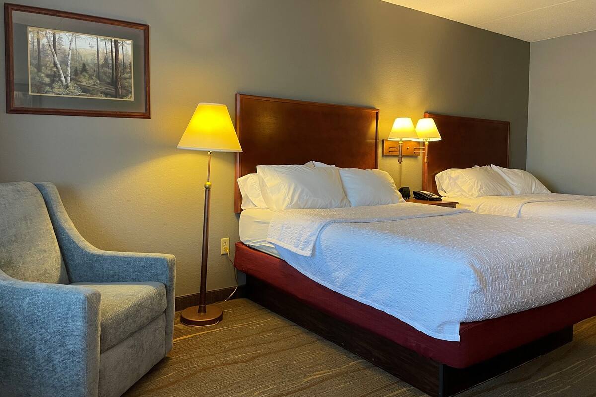 A hotel room with a double bed, a chair, a desk, and a lamp.