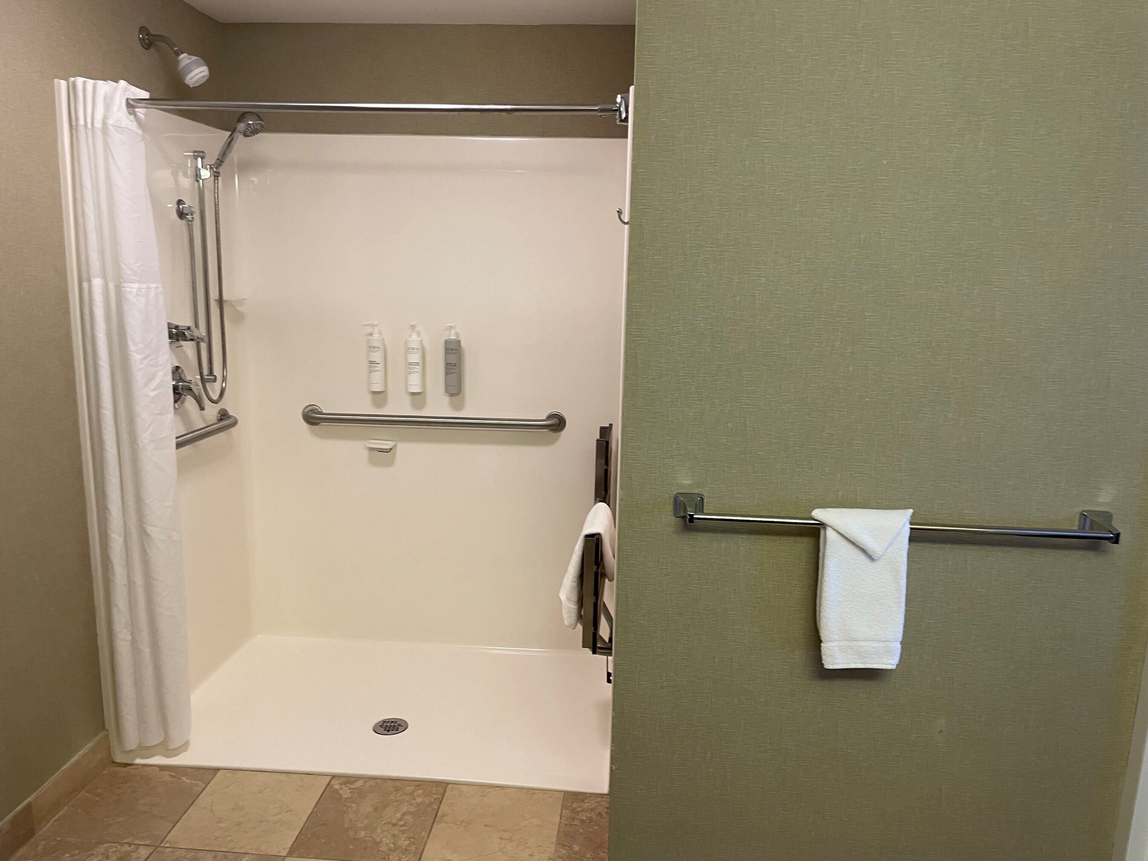 A shower area with a glass door, a towel rack, and toiletries on a shelf.