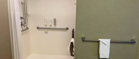 A shower area with a glass door, a towel rack, and toiletries on a shelf.
