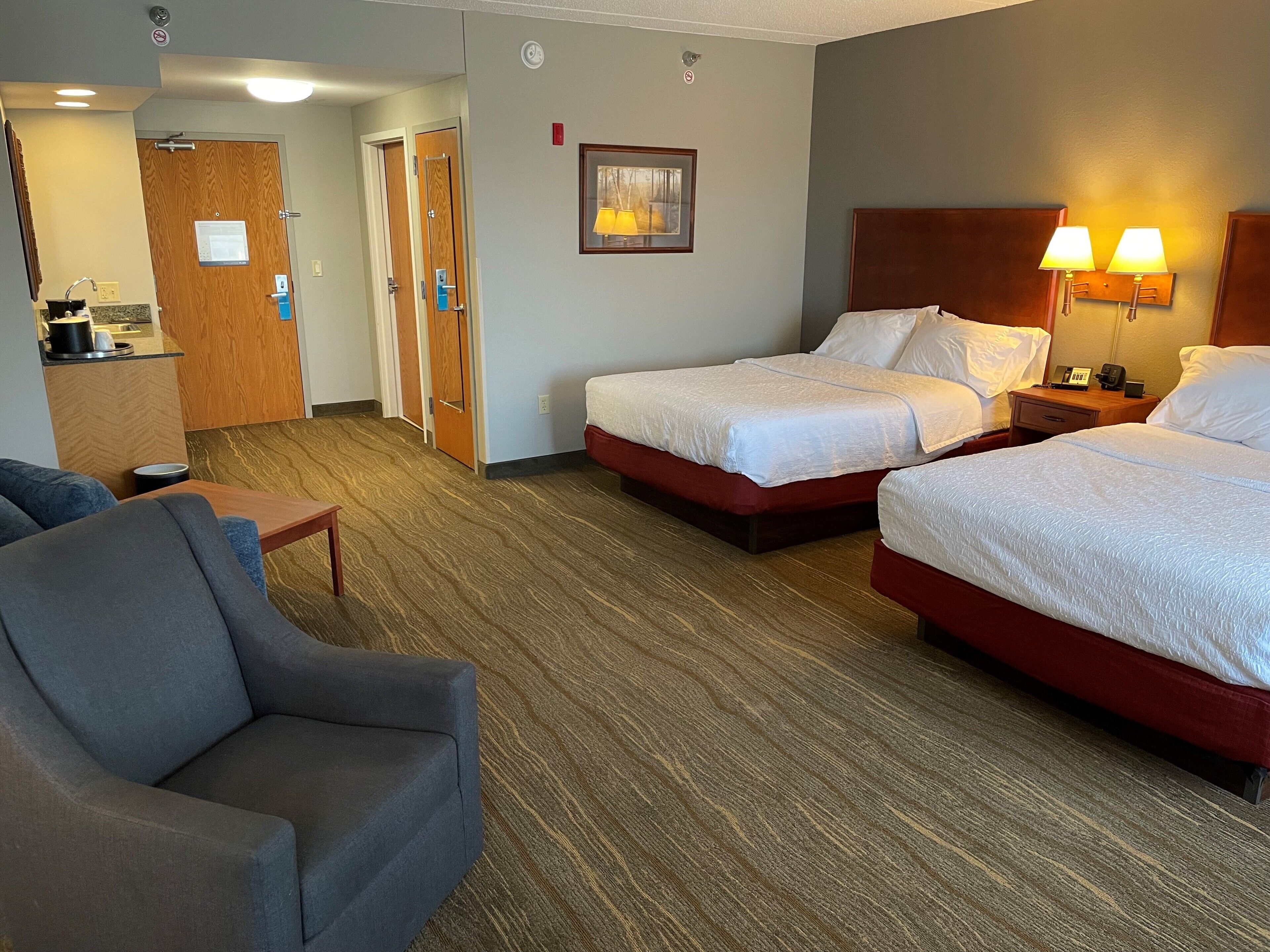 A hotel room with two beds, a sofa, a desk, and a small kitchenette.