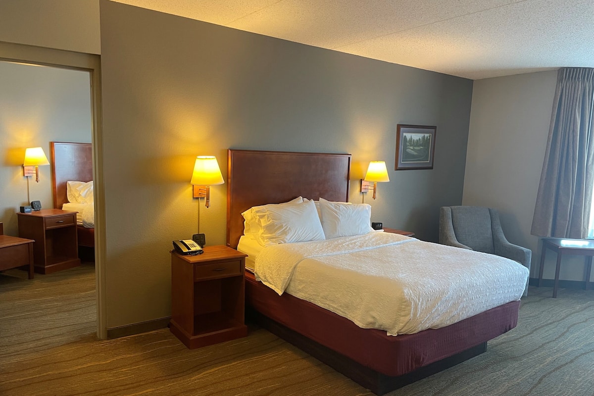A hotel room with a large bed, two bedside lamps, a chair, a desk, and a mirror.