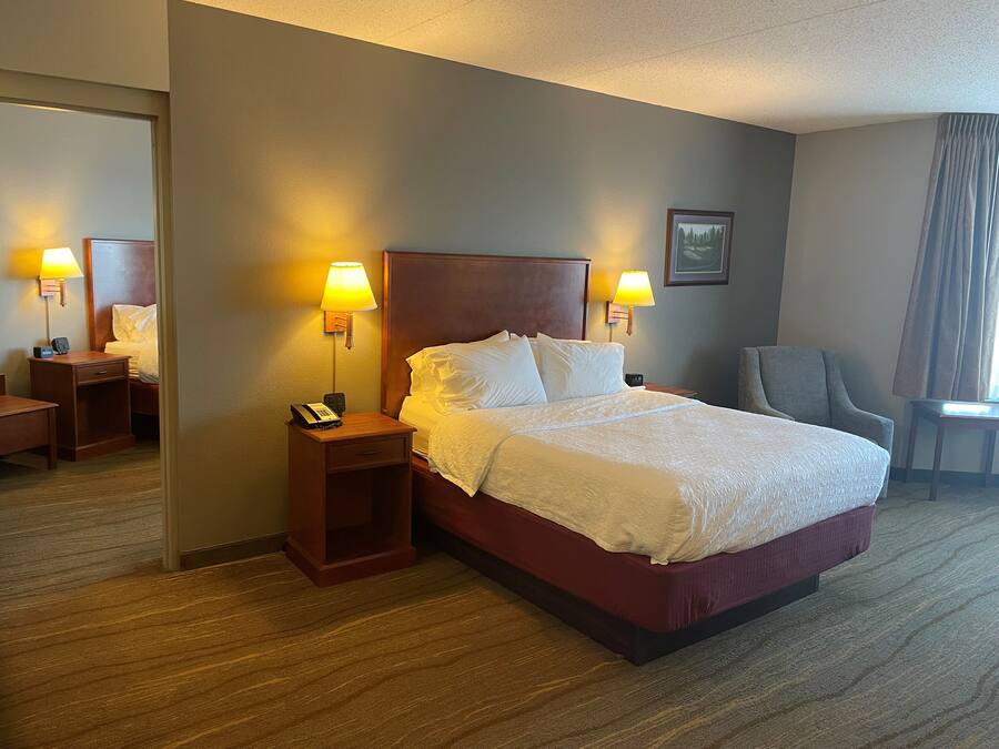A hotel room with a large bed, two bedside lamps, a chair, a desk, and a mirror.