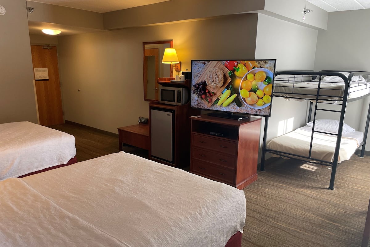 A hotel room with two beds, a TV, a desk, a microwave, and a bunk bed.