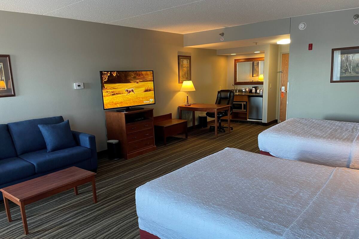 A hotel room with two beds, a sofa, a TV, a desk, and a kitchenette.