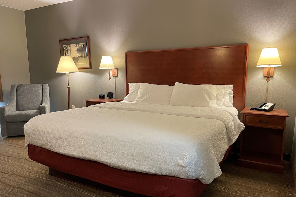 A hotel room with a large bed, two bedside tables, a chair, and two lamps.