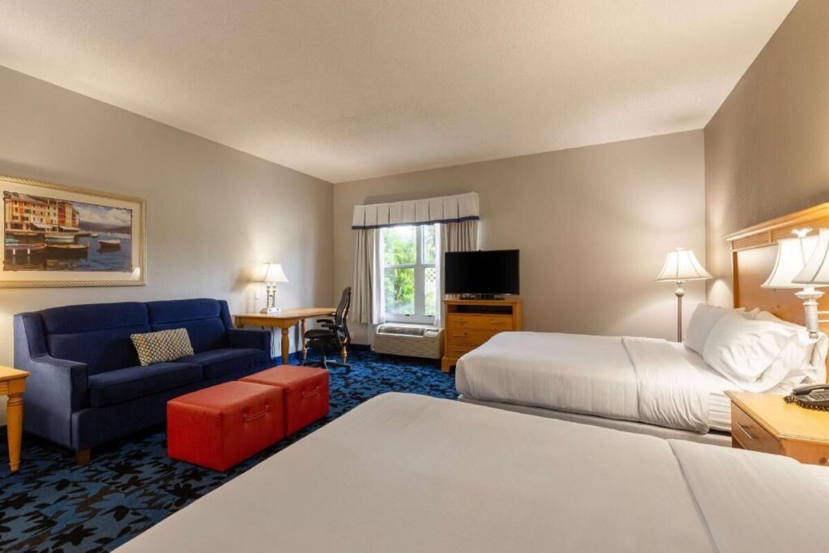 A hotel room with a bed, a sofa, a desk, a TV, and a window with curtains.