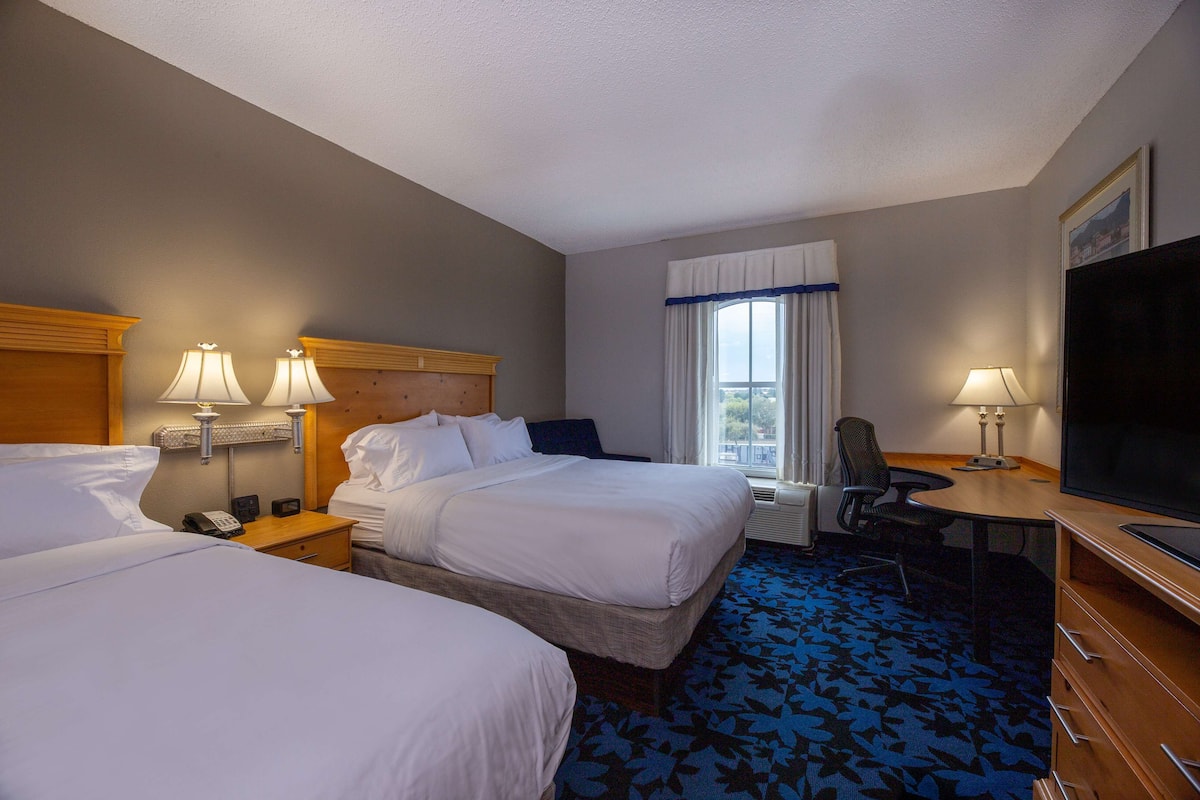 A hotel room with two beds, a desk, a TV, and a window with curtains.