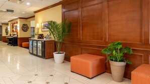 A hotel lobby with a reception desk, a coffee station, and potted plants.