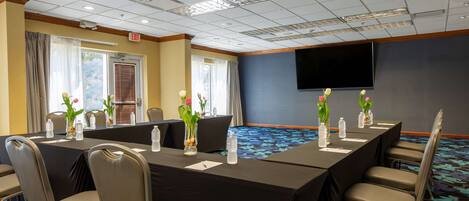 A conference room with a long table, chairs, and a TV on the wall.