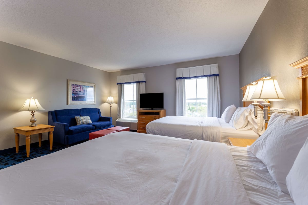 A hotel room with two beds, a sofa, a TV, and a lamp.